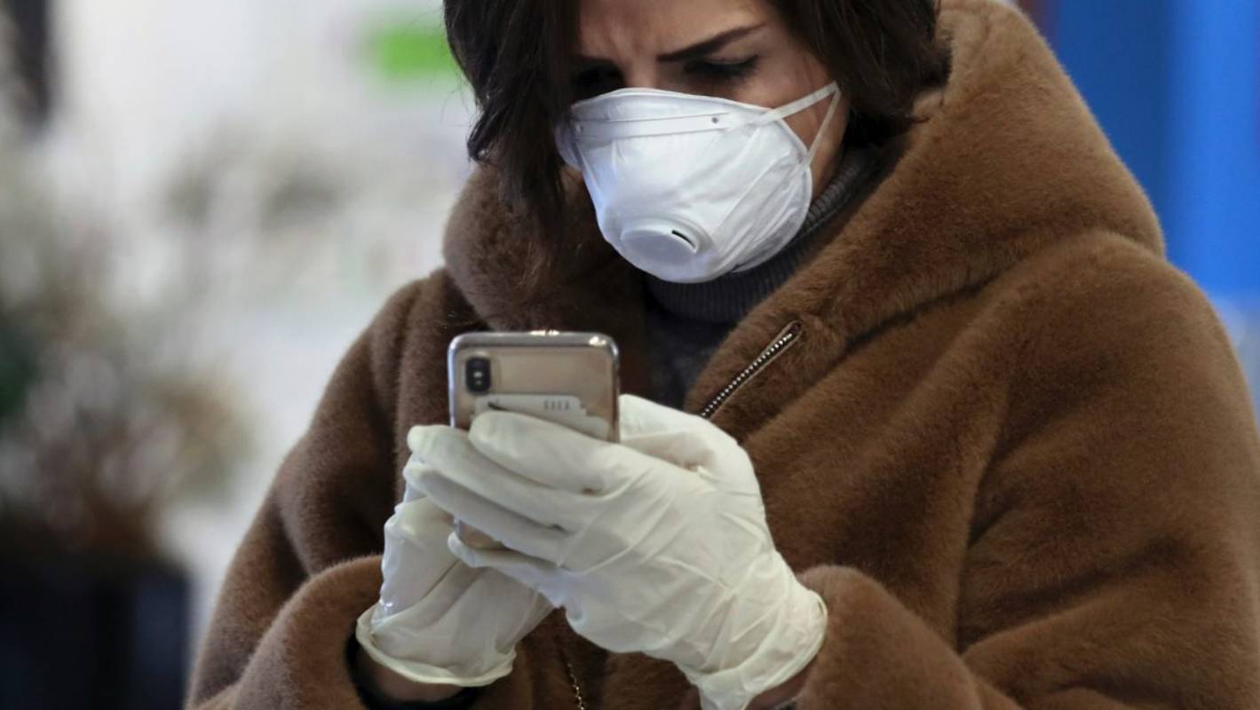persoana care poarta masca si utilizeaza telefonul