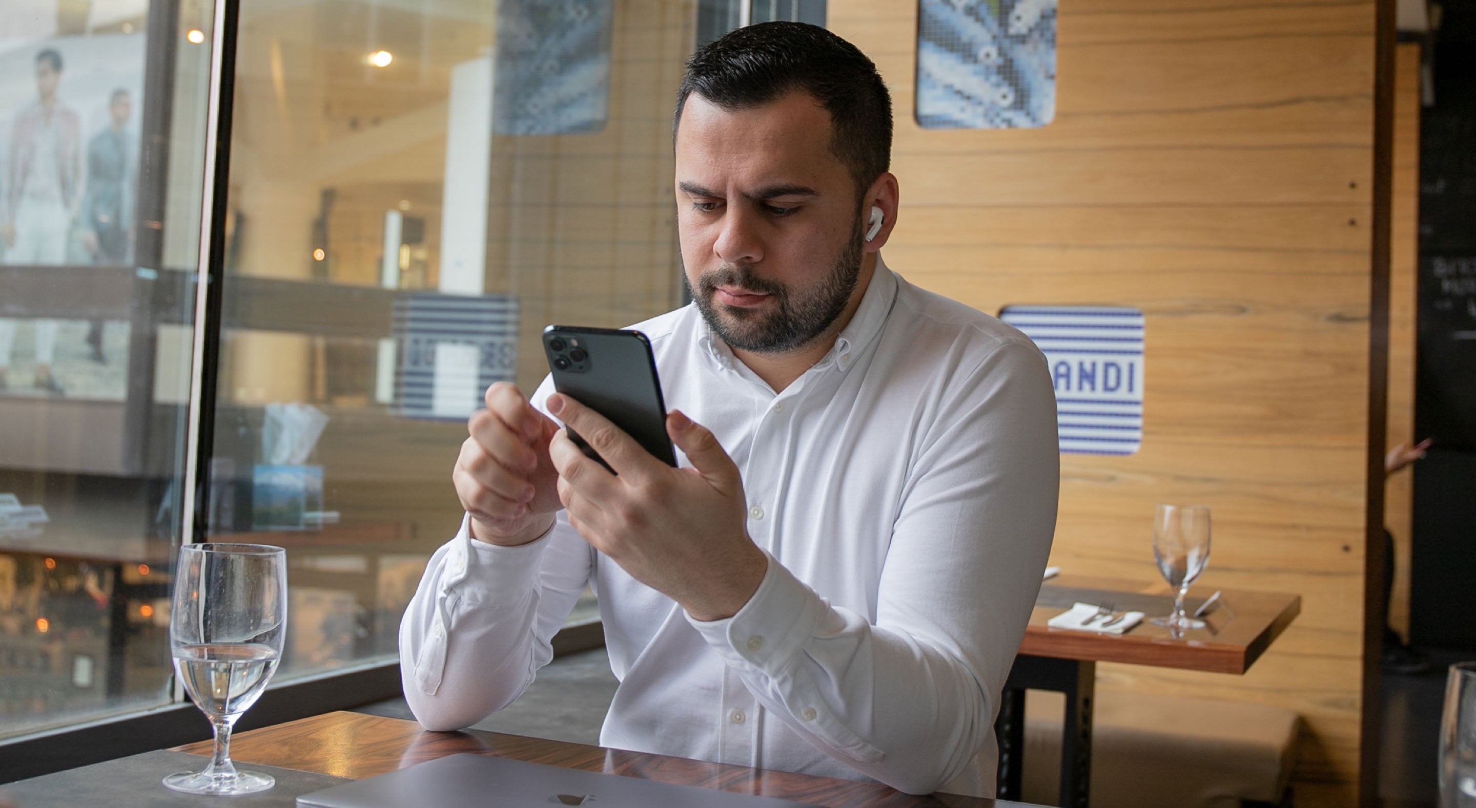 Slika čovjeka koji sjedi u restoranu i pregledava svoj iPhone